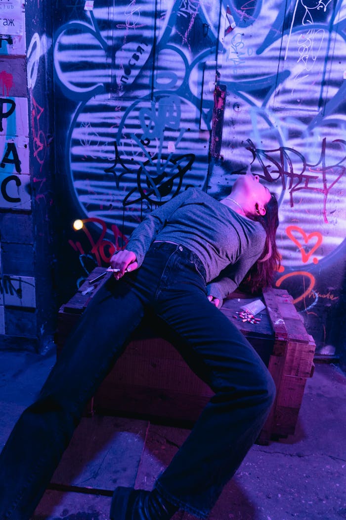 A person is reclining against a graffiti-covered wall at night.